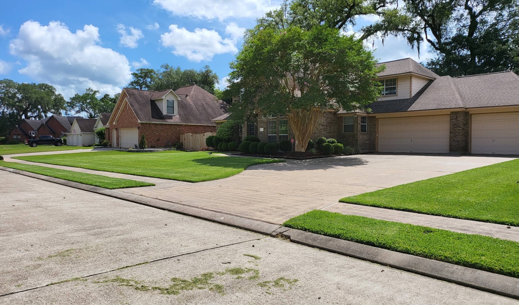 A summer front lawn at a two-storey brick home, cut and edged in a clean line along the concrete driveway and sidewalk