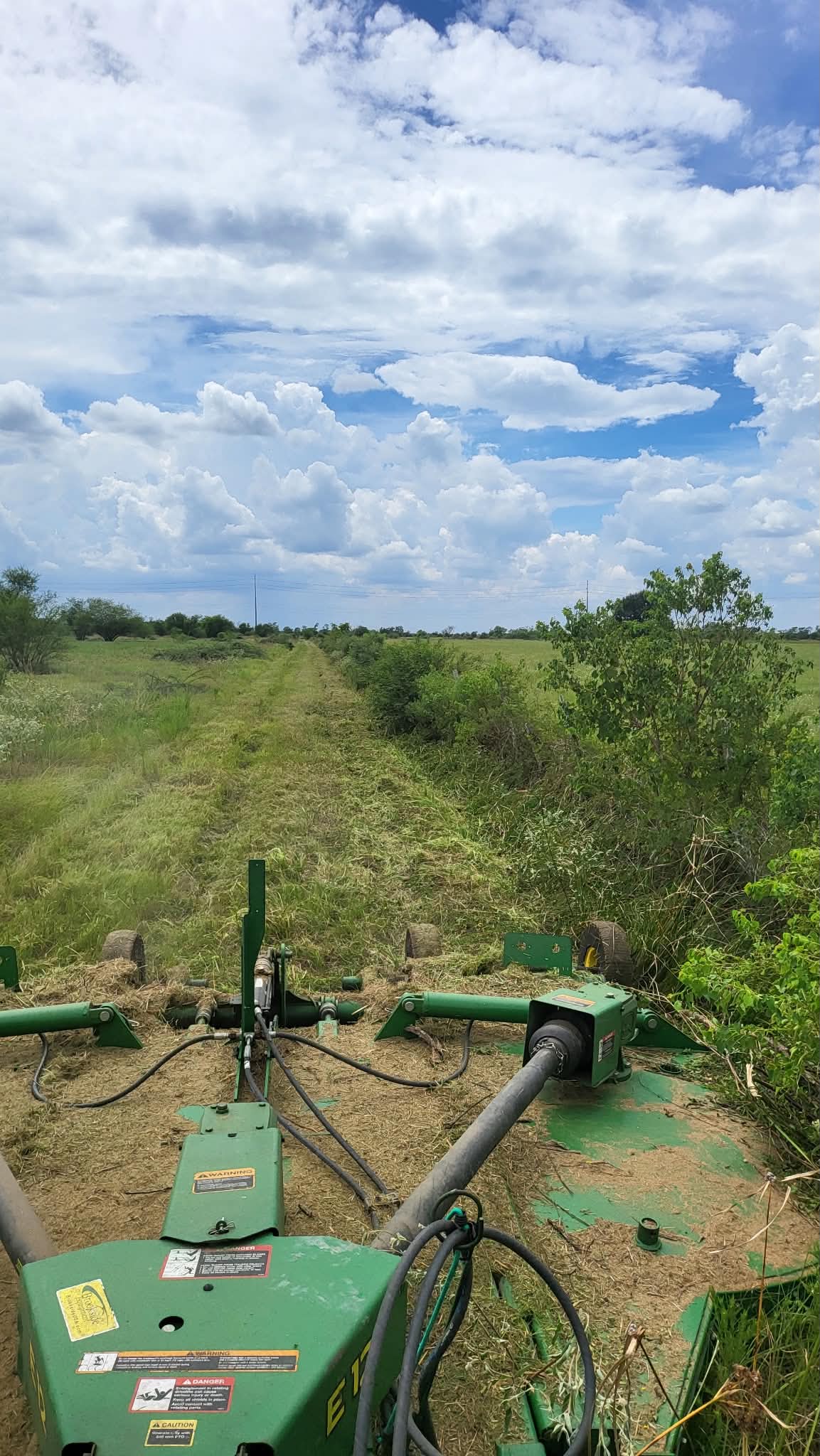 Looking out over the folded green batwing deck at a lane cut straight through heavy brush, open pasture either side